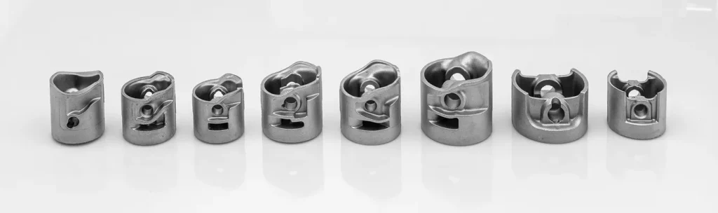 Eight aluminum die cast pistons in different sizes lined up on a white background